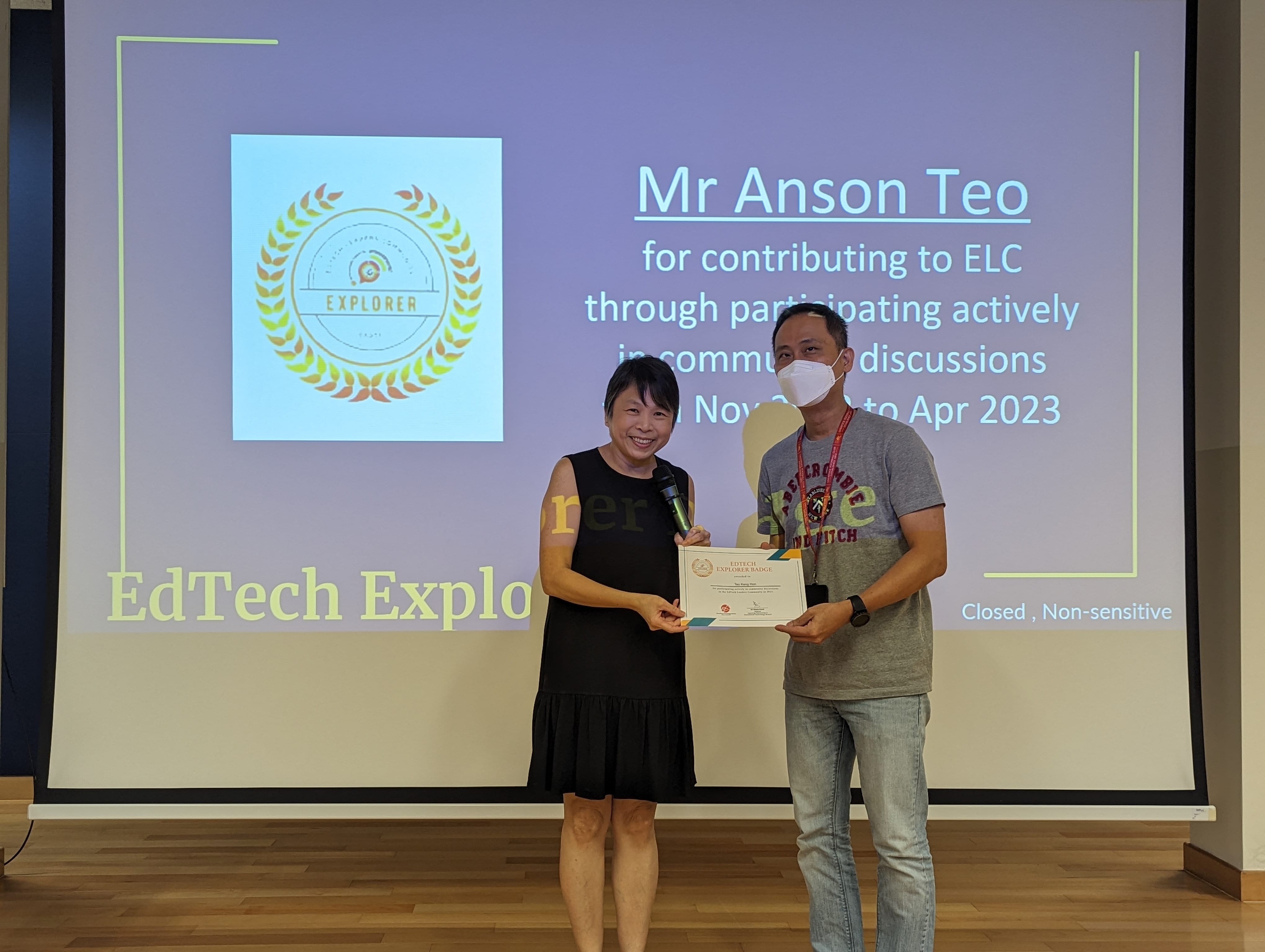Two people hold a certificate in front of a screen recognizing Mr Anson Teo for EdTech Explorer contributions.